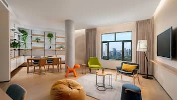 Un salon moderne comprenant un coin repas, une grande fenêtre offrant une vue sur la ville, un téléviseur à écran plat fixé au mur, et divers types de sièges, notamment un fauteuil poire, des chaises et un canapé.