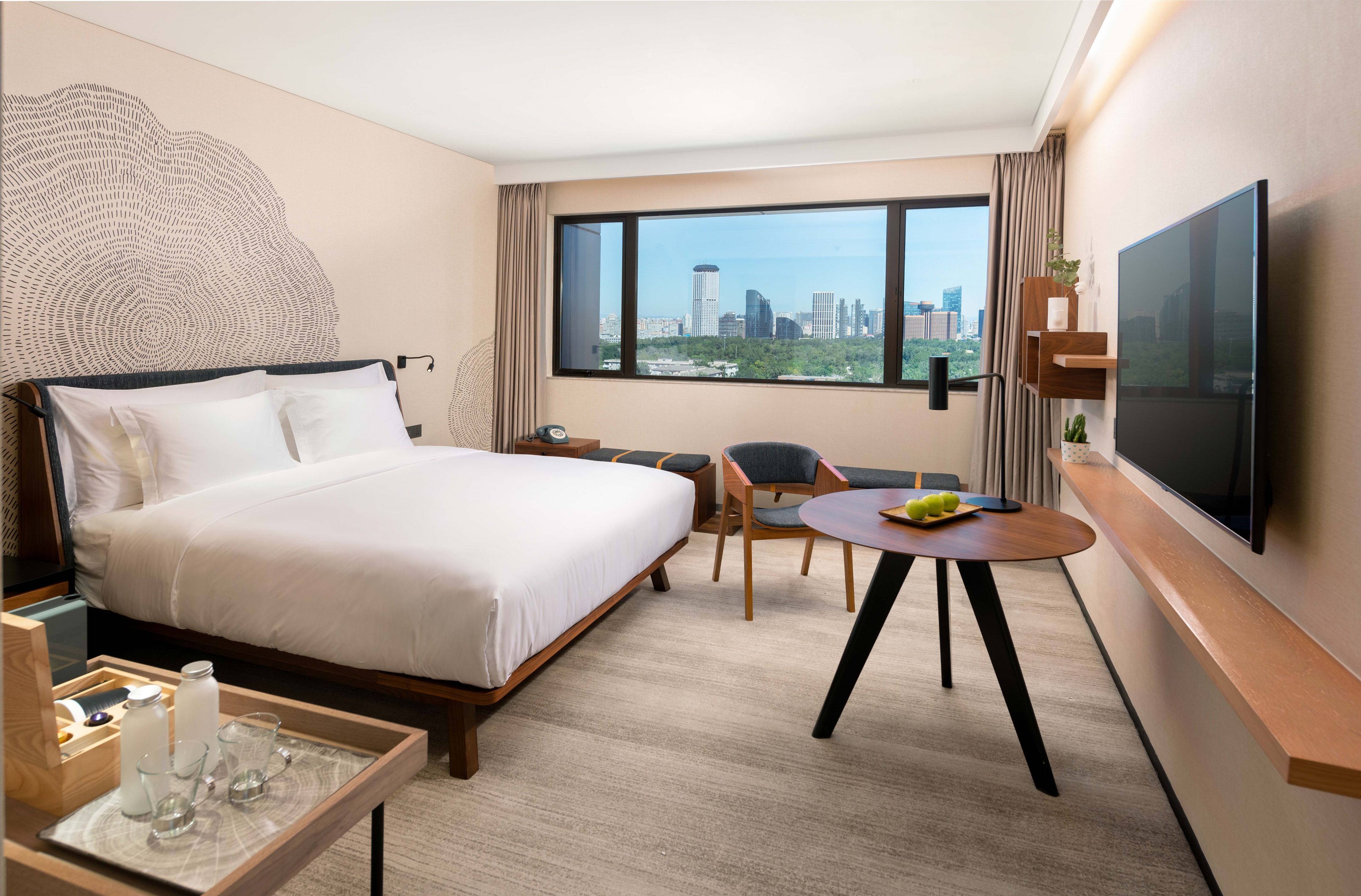 Une chambre d’hôtel avec un lit, un bureau et une chaise, une télévision et une vue sur le paysage urbain.