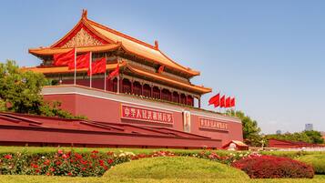 A traditional Chinese building with multiple flags, surrounded by well-maintained gardens and a clear sky.