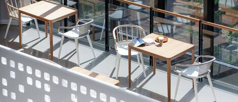 Un espacio exterior moderno con mobiliario de madera y sillas de metal, delimitado por barandas de vidrio.