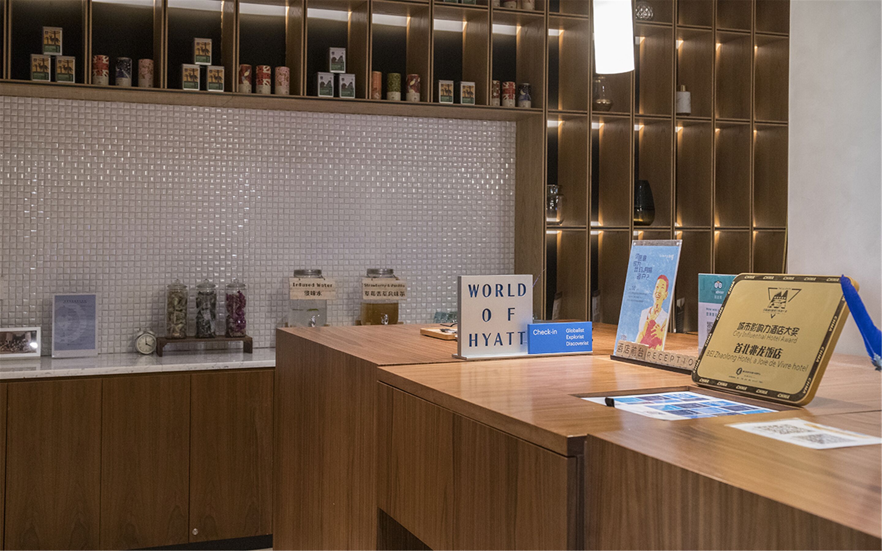 A reception desk with a "World of Hyatt" sign, a "Check in" sign, and a "Reception" sign. There are jars labeled "Infused Water" and "Syrup & Powder".