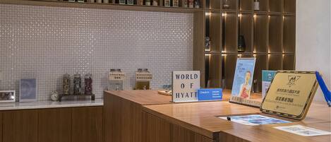 A reception desk with a "World of Hyatt" sign, a "Check in" sign, and a "Reception" sign. There are jars labeled "Infused Water" and "Syrup & Powder".