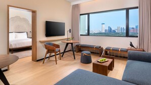 A modern hotel room with a bed, a TV, a dining area, and a large window with a city view. - BEI Zhaolong Hotel, part of JdV by Hyatt (Beijing)