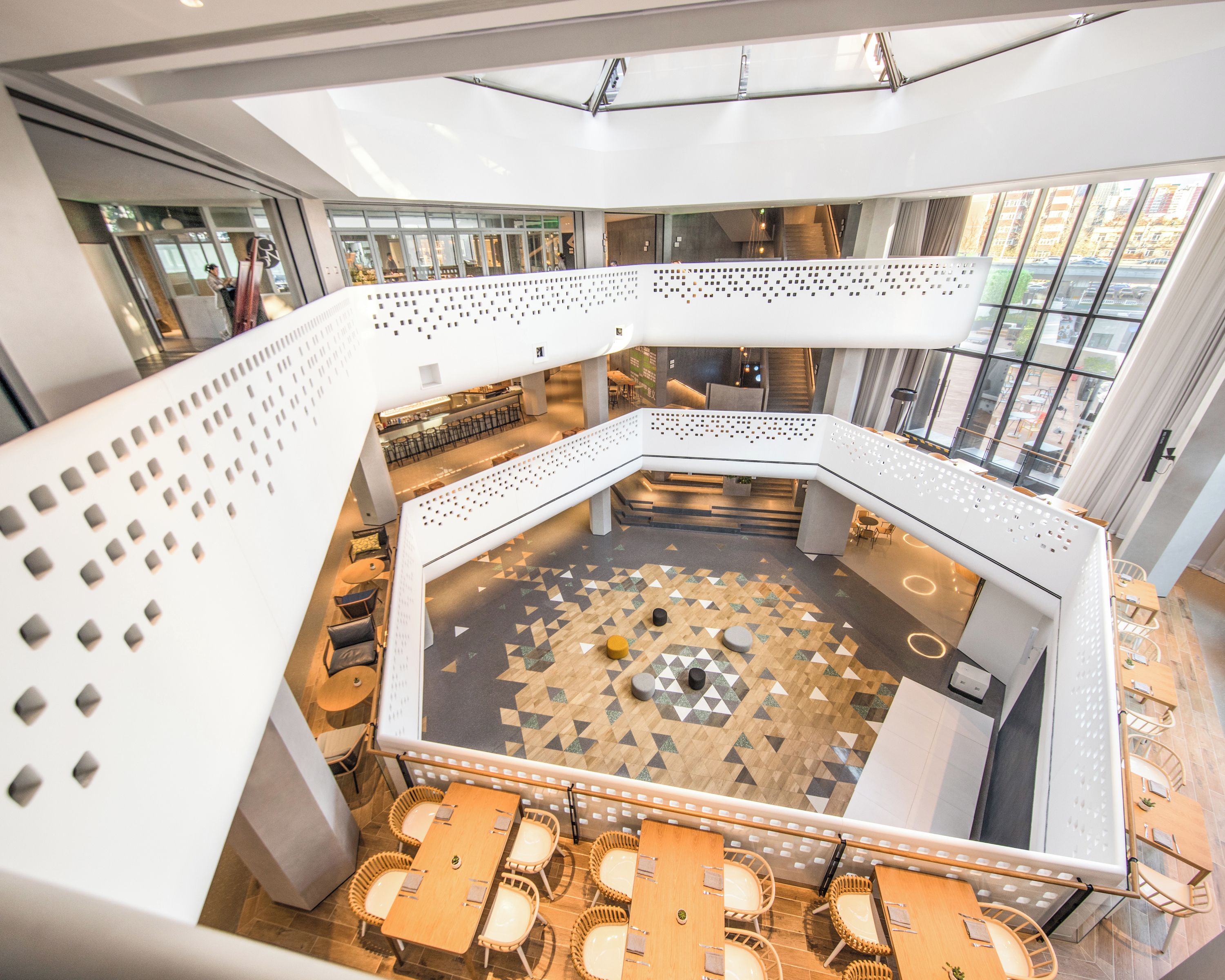 A spacious atrium with a high ceiling, a central seating area with tables and chairs, and large windows providing views of the outside.