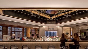 A modern bar area with a high ceiling, a bar counter with various bottles, and several bar stools. - BEI Zhaolong Hotel, part of JdV by Hyatt (Beijing)
