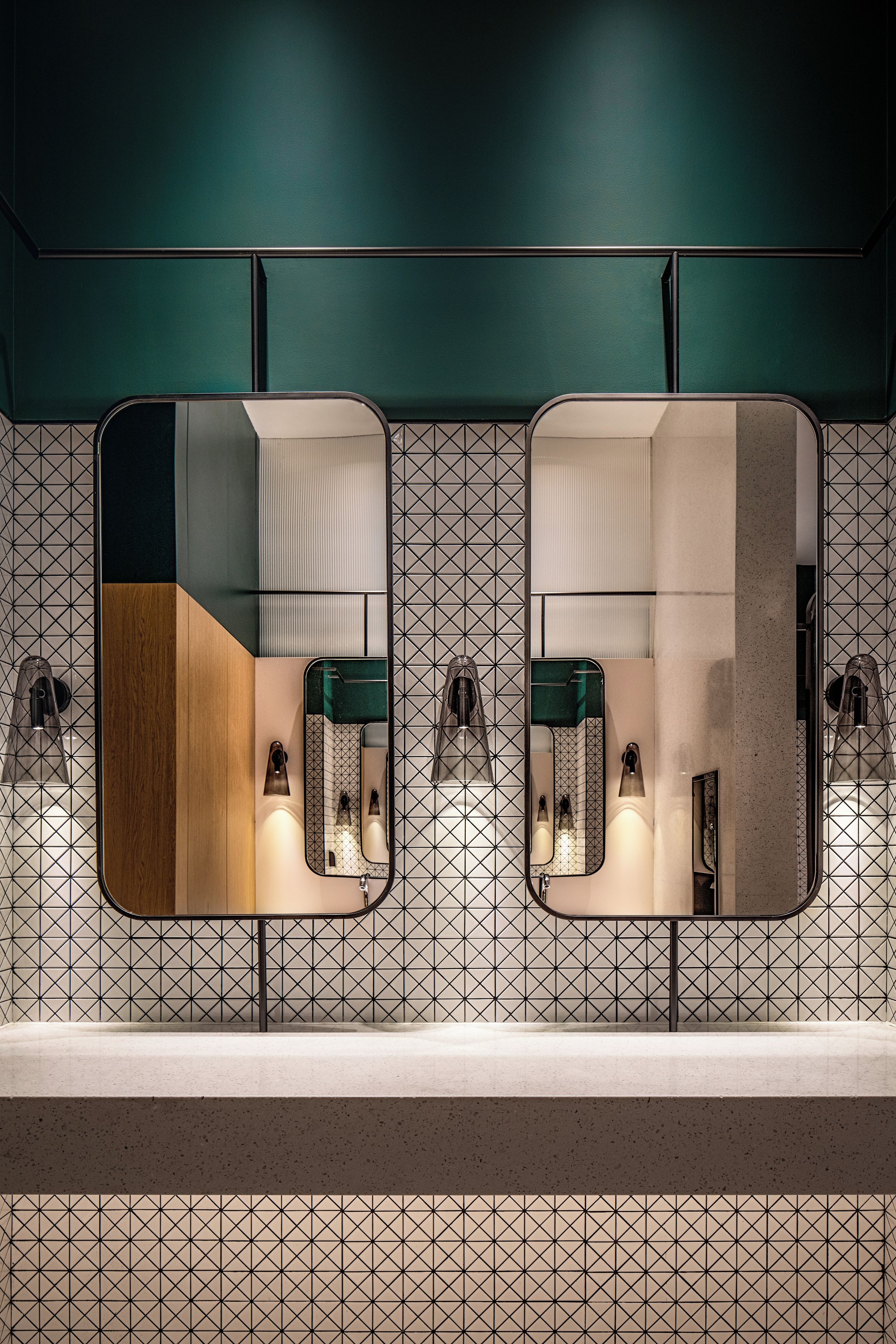 Ein Badezimmer mit zwei Waschbecken, einem Spiegel und einer Wand mit geometrischen Fliesen.
