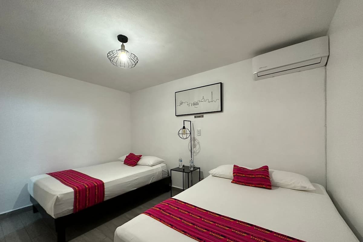 A hotel room with two single beds, a nightstand, a wall-mounted air conditioner, and a cityscape artwork.