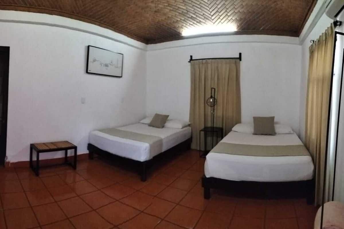 A room with two beds, a small table, a water bottle, and a picture on the wall.