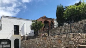 Un patio con un edificio blanco, un muro de piedra y una escalera que lleva a una construcción de techo rojo.