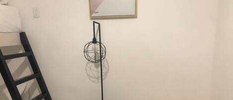 Una habitación con una escalera negra apoyada en la pared, una mesa de metal negro con base negra, y un banco de madera con estructura negra.