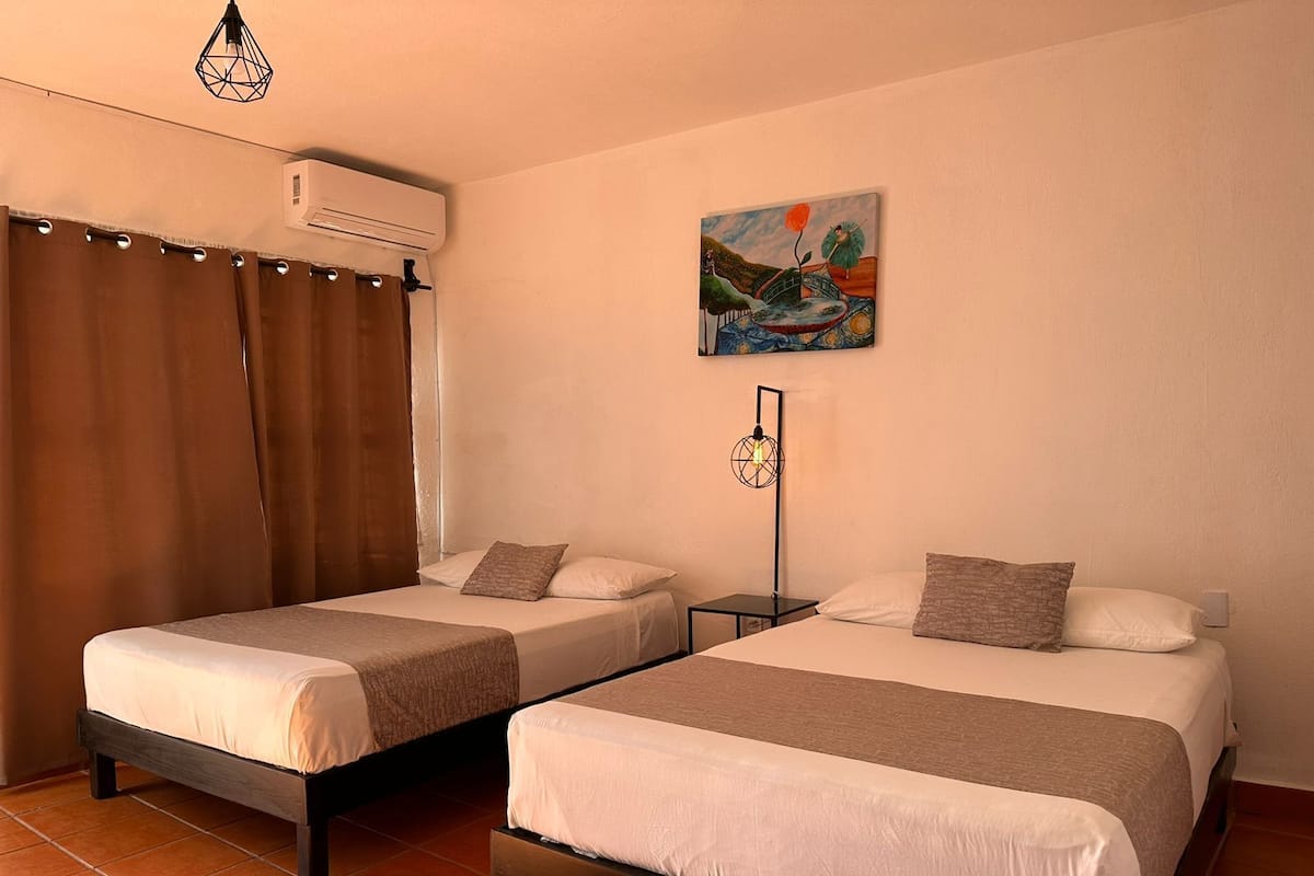 A hotel room with two beds, a painting on the wall, and an air conditioning unit.