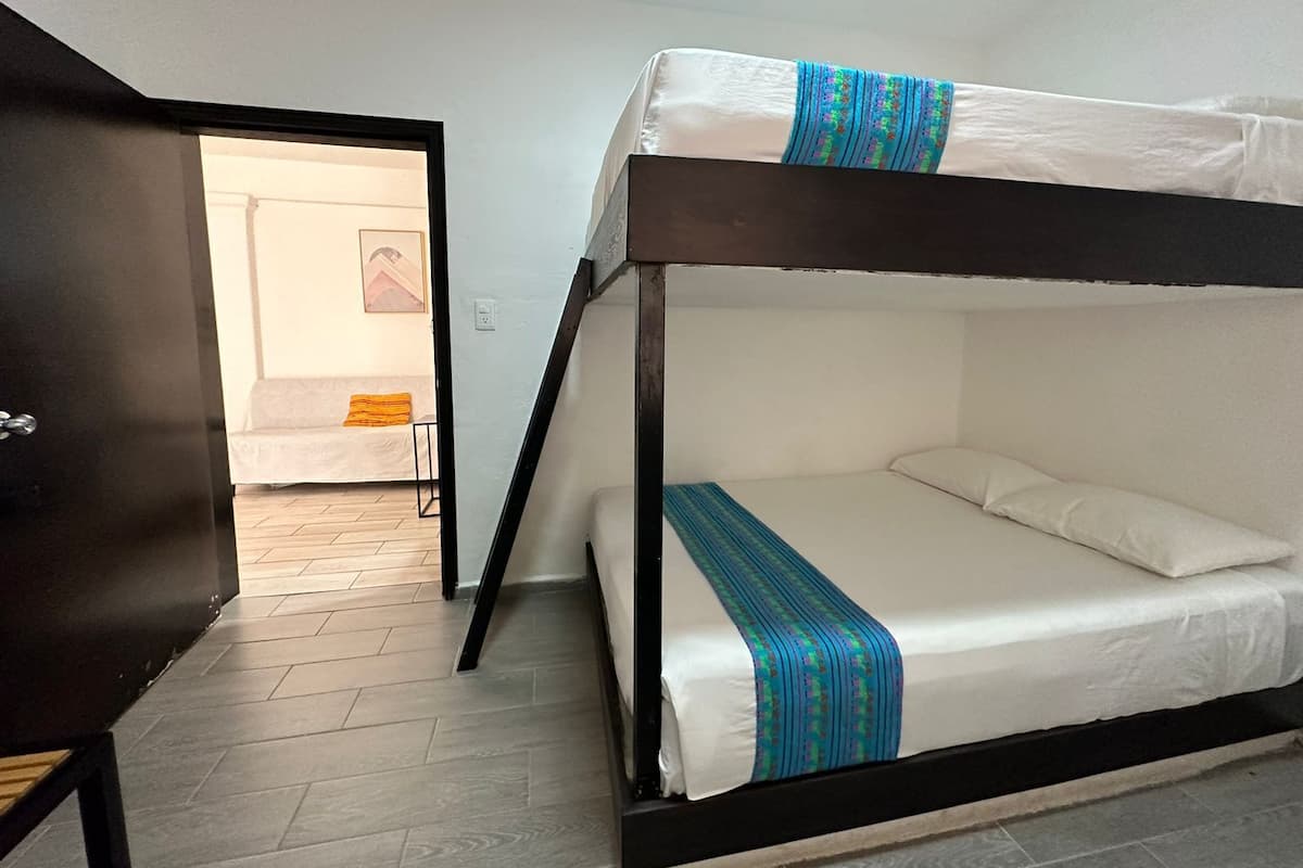 A bunk bed room with a wooden floor, a desk, and a door leading to another room.