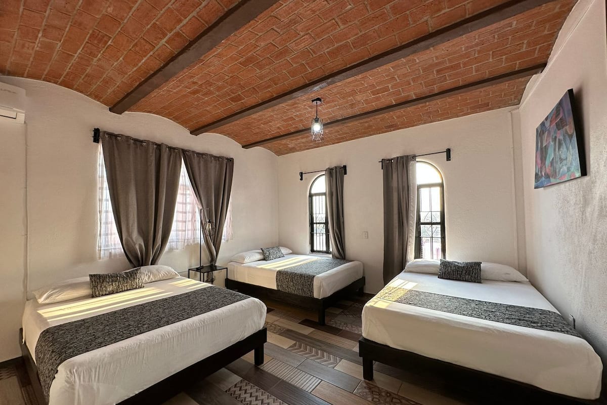 A room with three beds, a brick ceiling, and patterned flooring.