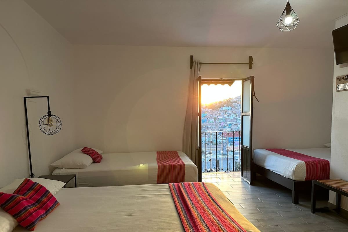 A hotel room with two beds, a balcony with a view, a hanging light fixture, and a wall-mounted sign indicating WiFi availability.