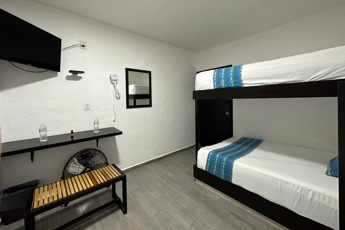 A room with a bunk bed, a small table with a fan, a mirror, and a hairdryer on the wall.