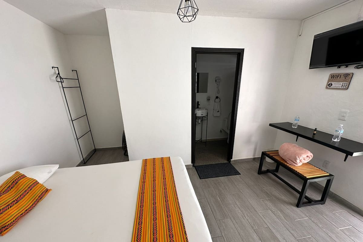 A hotel room with two beds, a bench, a TV, a minibar, and a door leading to a bathroom.