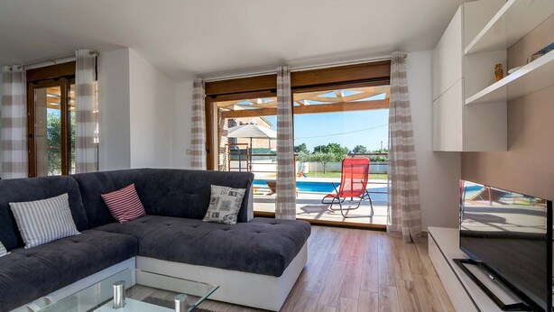 Un salón moderno con sofá, televisión y vistas a una piscina.
