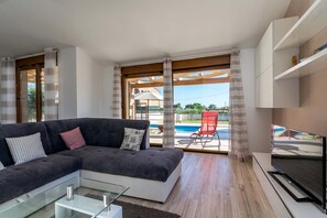 Ett modernt vardagsrum med en soffa, en tv och utsikt över en swimmingpool.