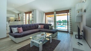 Una sala de estar moderna con un sofá modular, una mesa de centro de vidrio y vistas a una piscina a través de amplios ventanales.