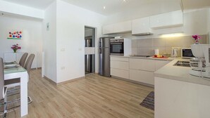 Una cocina moderna con armarios blancos, electrodomésticos de acero inoxidable y una zona de comedor con mesa y sillas.