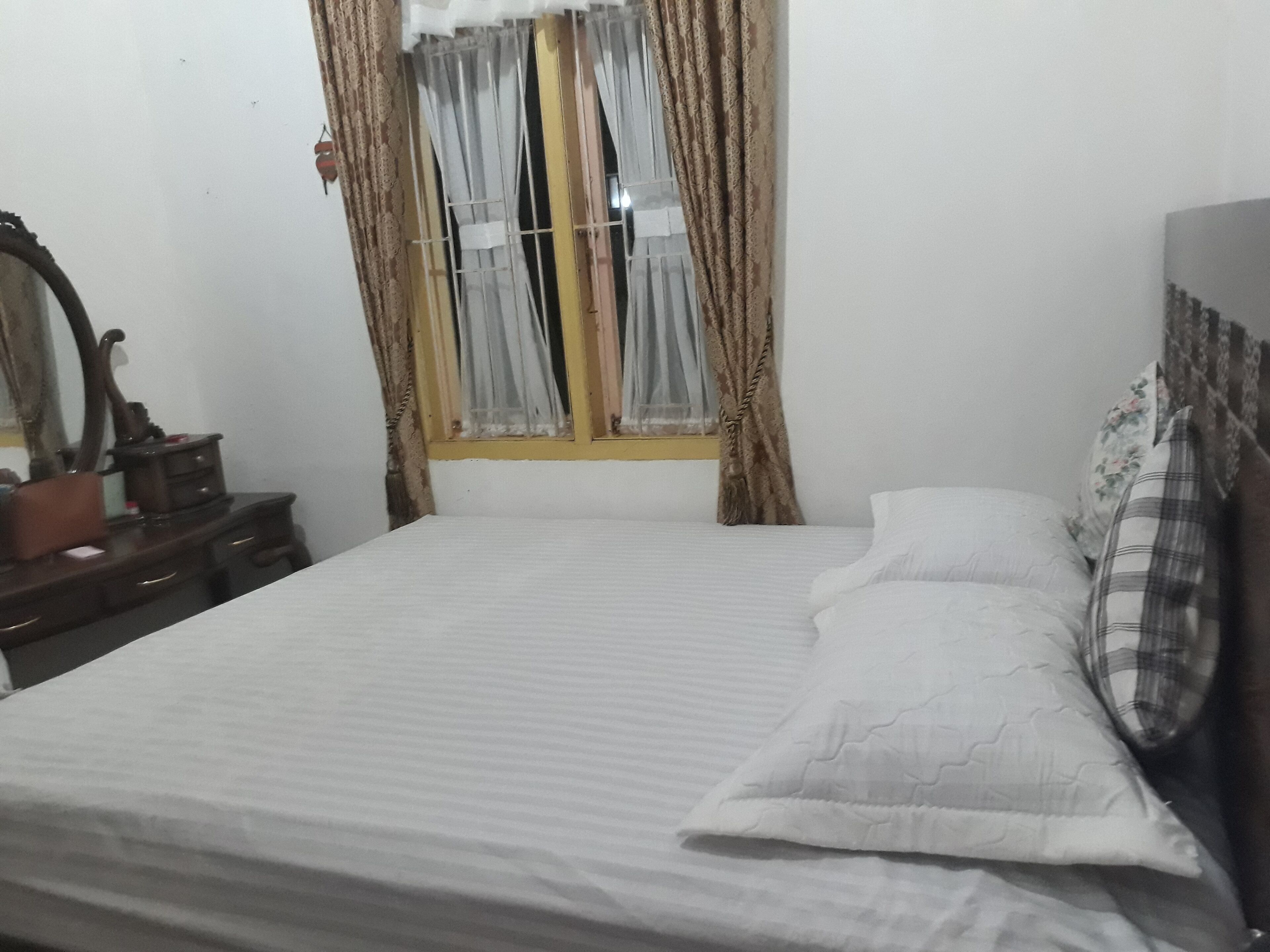 Ein Schlafzimmer mit einem Einzelbett, einem Schminktisch, einem Spiegel und einem Fenster mit Vorhängen.