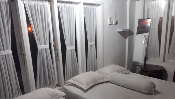 A hotel room with two beds, white linens, a bedside table, a lamp, and curtains.