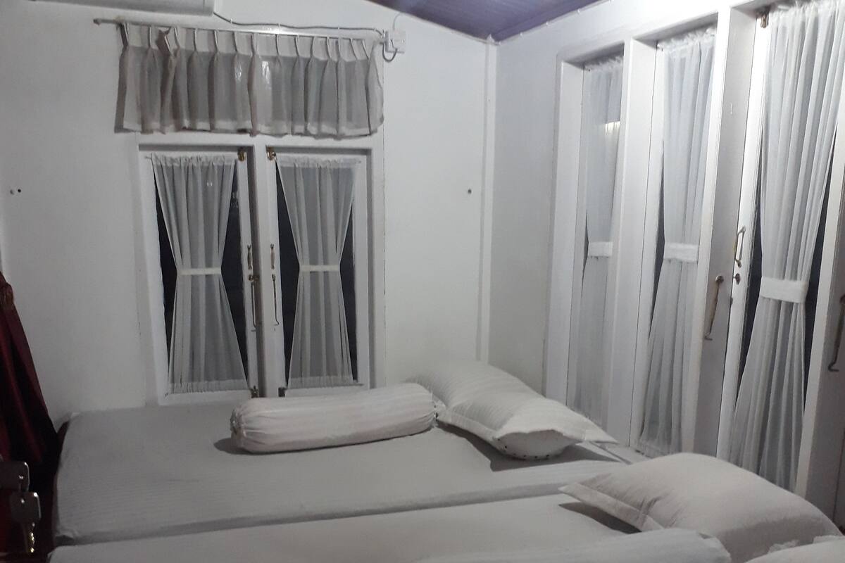 A room with two beds, white bedding, a ceiling fan, and curtains.