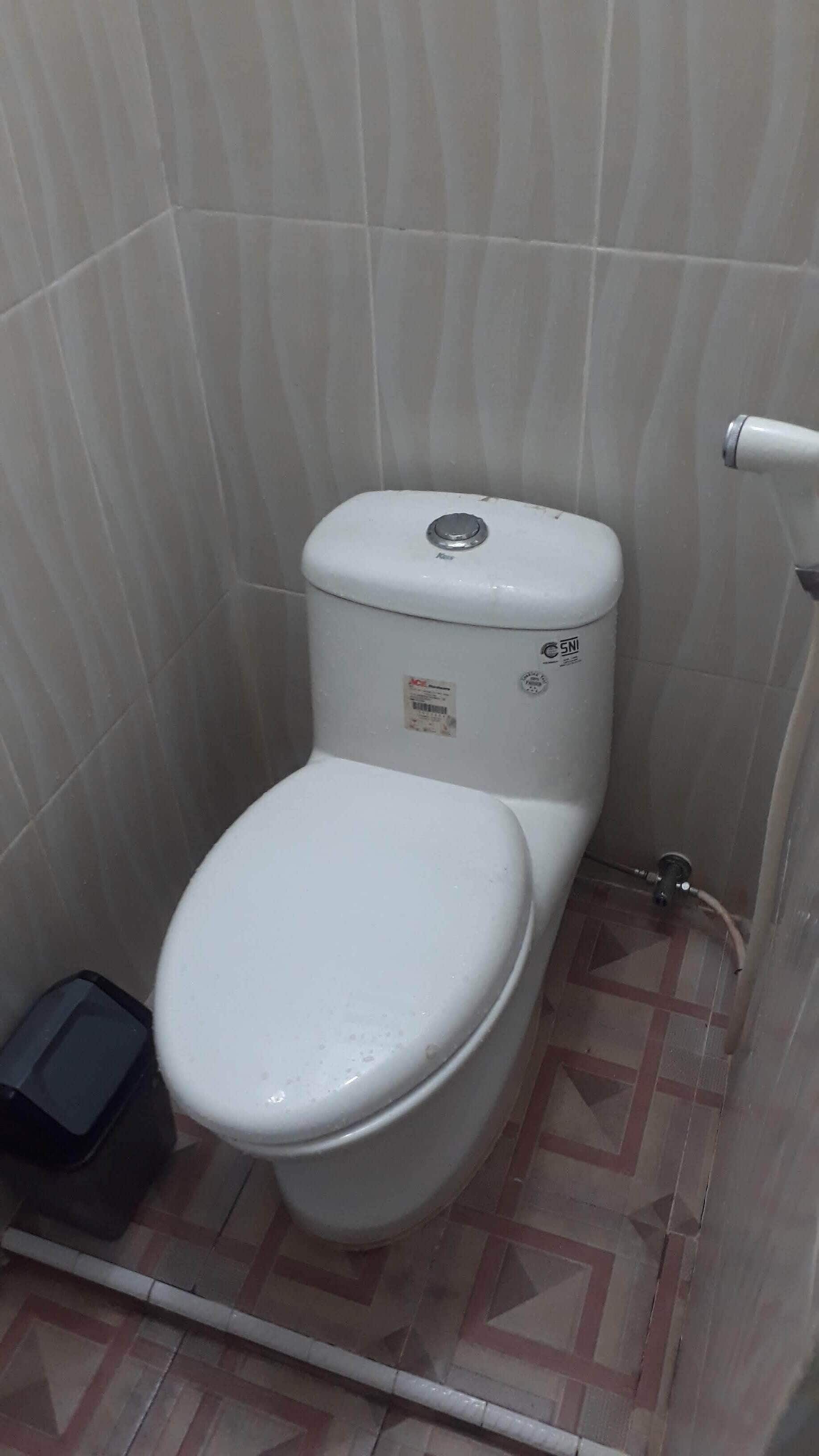 Ein kleines, kompaktes Badezimmer mit Toilette, sichtbarem Wassertank und Fliesenboden.