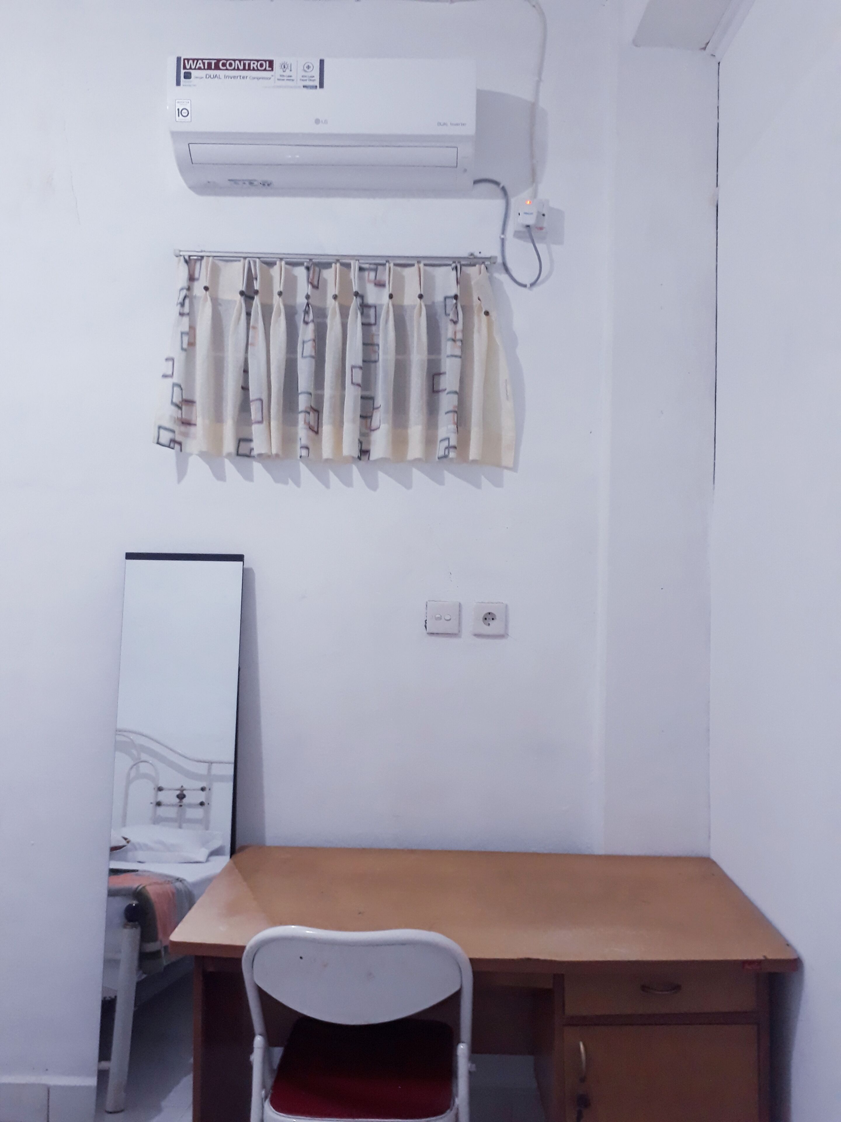 Ein Zimmer mit einem Holztisch, einem weißen Stuhl, einer Wand-Klimaanlage, einem Heizkörper und einem Bett mit Kopfteil.