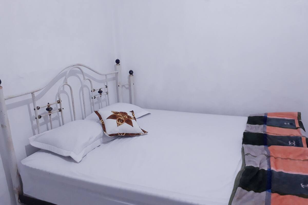 A white metal bed with a white mattress and two pillows, one with a gold pattern.