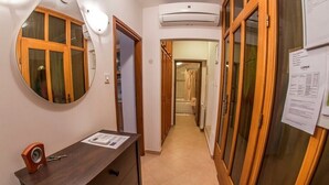 Un pasillo estrecho con un escritorio de madera, un espejo y una puerta que da a un baño.