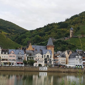 A historic town with a prominent tower and a sign reading "ZELL" by a calm river.