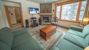 A living room with a fireplace, green upholstered sofas, a wooden coffee table, and a television mounted on the wall. - Cozy Townhome walk to River Run, Dining, Shops (Keystone)
