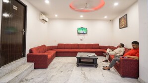 A modern living room with a red sectional sofa, a coffee table, and a television mounted on the wall. -  Hotel Smart by Kelvish Hotel (New Delhi)