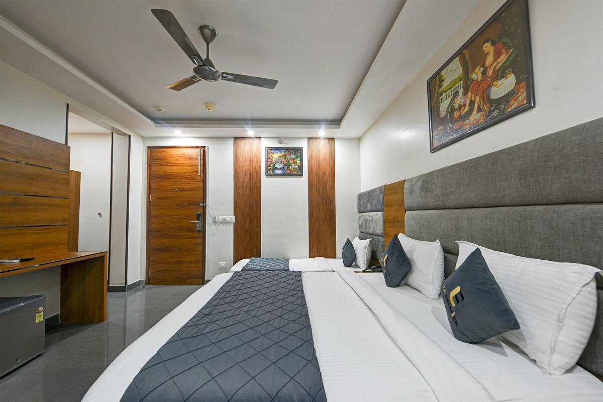 Quarto de hotel com cama, escrivaninha, guarda-roupa, ventoinha no teto e um quadro na parede.
