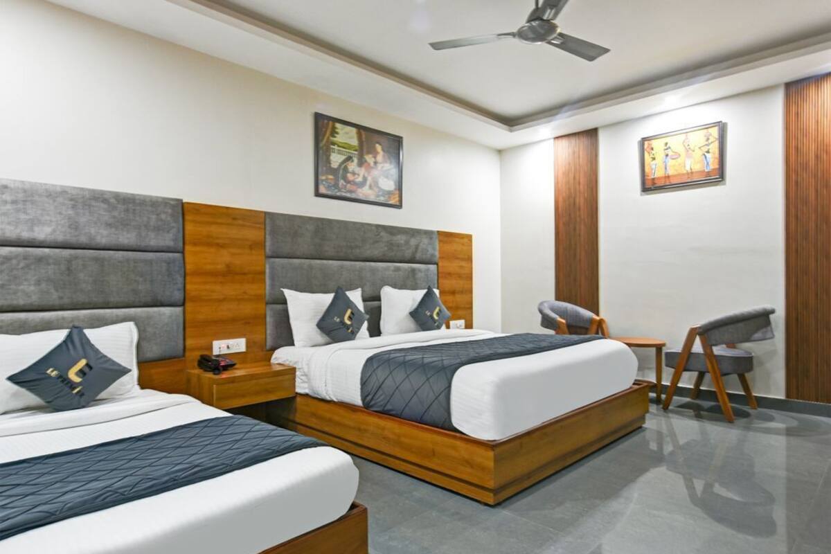 Quarto de hotel com duas camas, uma escrivaninha, uma cadeira, ventoinha no teto e obras de arte nas paredes.