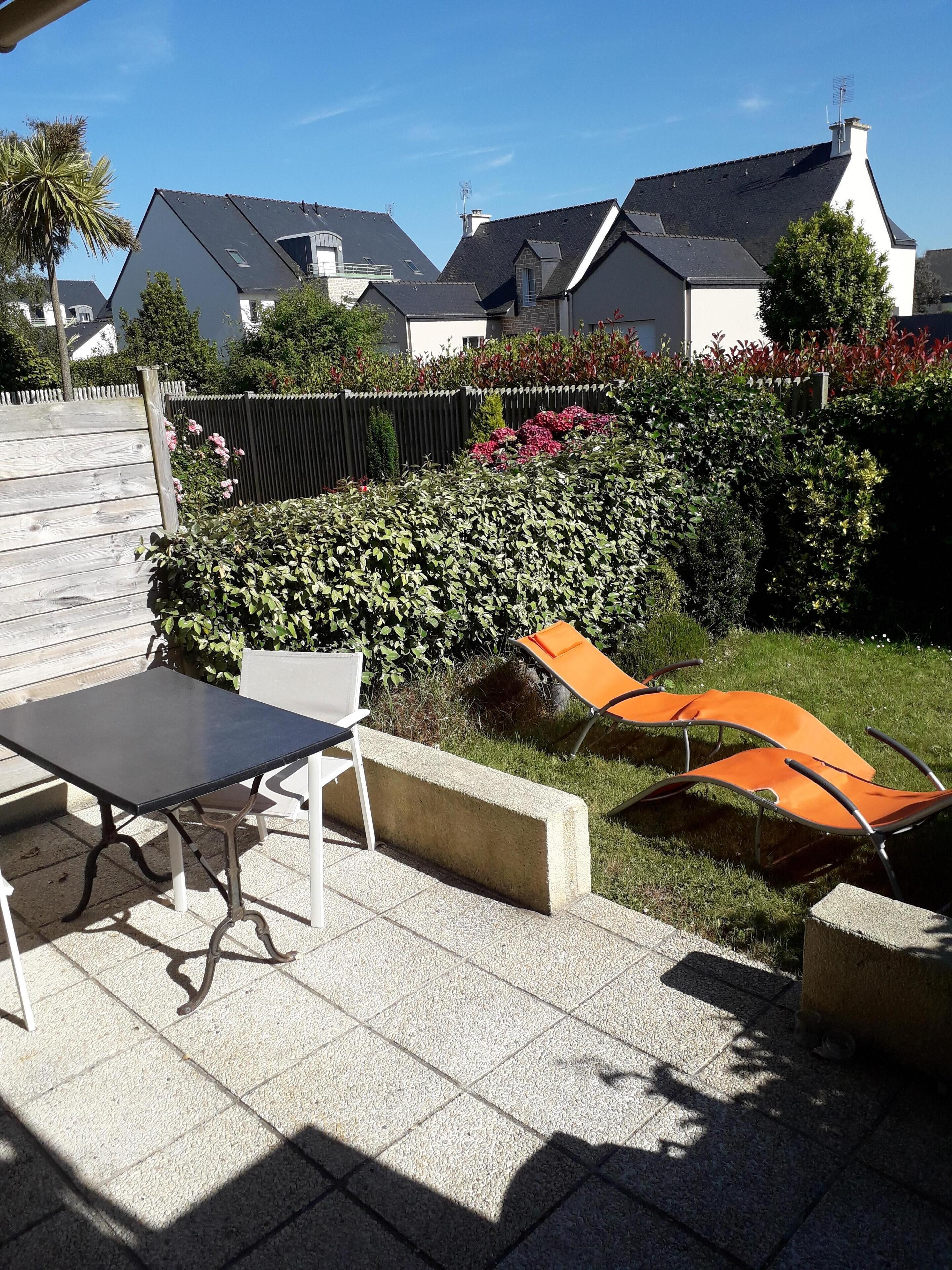 Un patio al aire libre con una mesa y sillas, un bloque de concreto y un seto en el fondo.