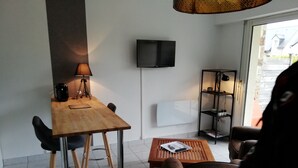 A modern living room with a wooden table, two chairs, a coffee table, a TV mounted on the wall, and a bookshelf. - Studio with garden at the doors of the beach and thalasso ROSCOFF (Roscoff)