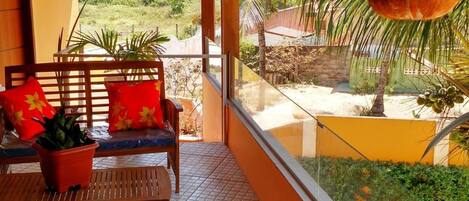 A balcony with wooden furniture, potted plants, and a view of greenery outside.