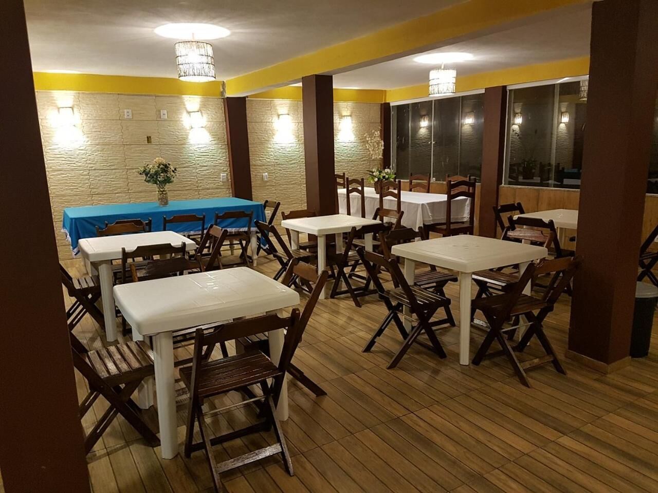 A restaurant with wooden flooring, white tables, and brown chairs.