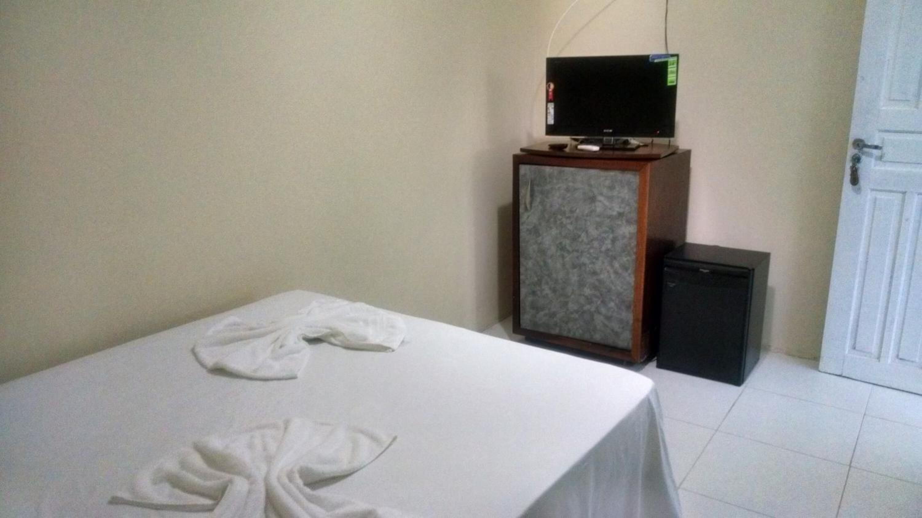 Une chambre d’hôtel avec un lit, un téléviseur posé sur une commode en bois et un petit appareil noir.
