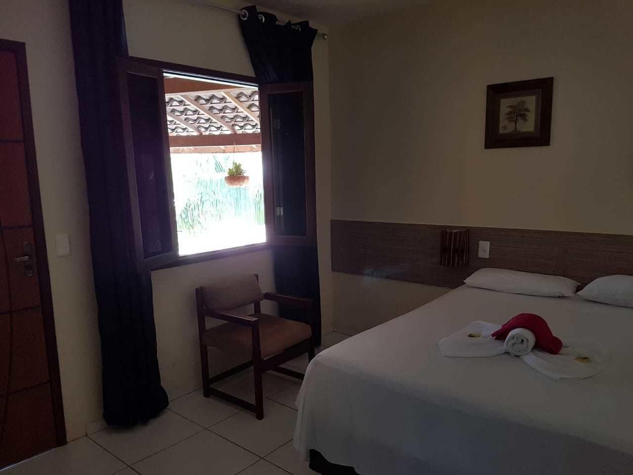 Una habitación de hotel con cama, una silla, una ventana con cortinas y un cuadro colgado en la pared.