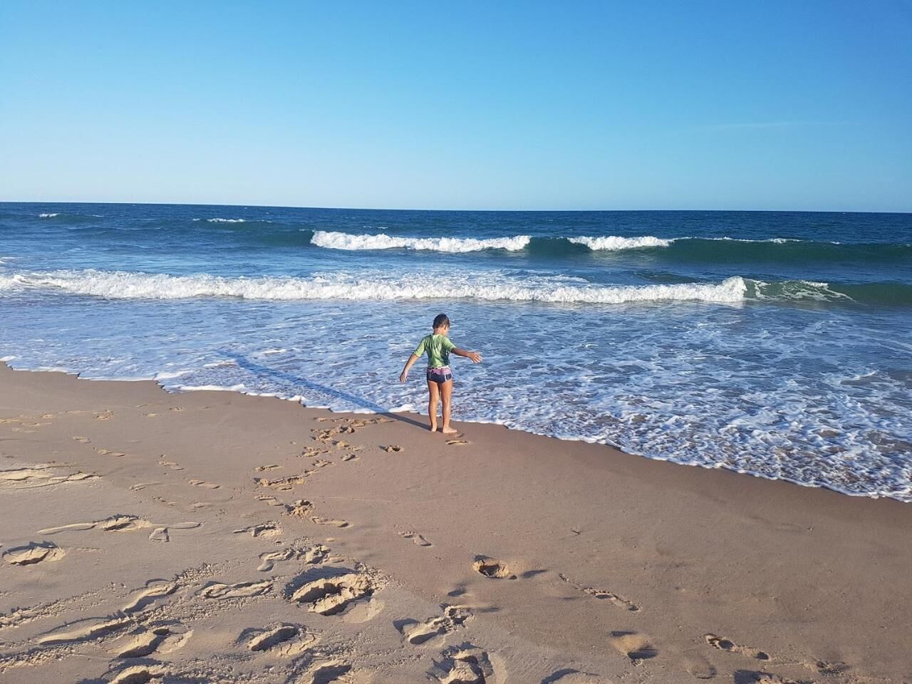 En person står på en sandstrand med fodaftryk, der går ud i vandet.