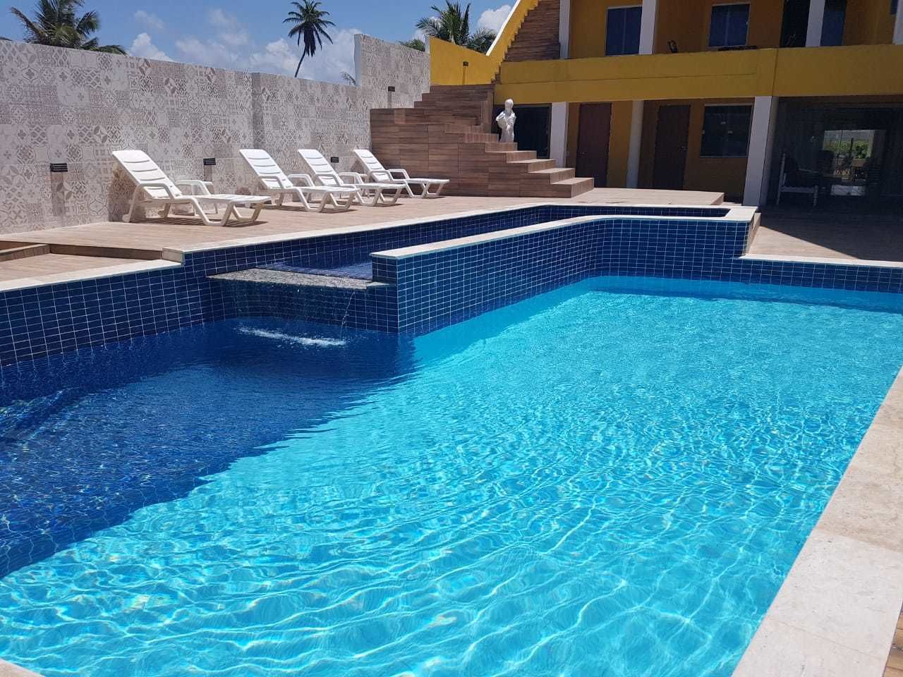 A swimming pool with clear blue water, white lounge chairs, and a staircase leading to a building.