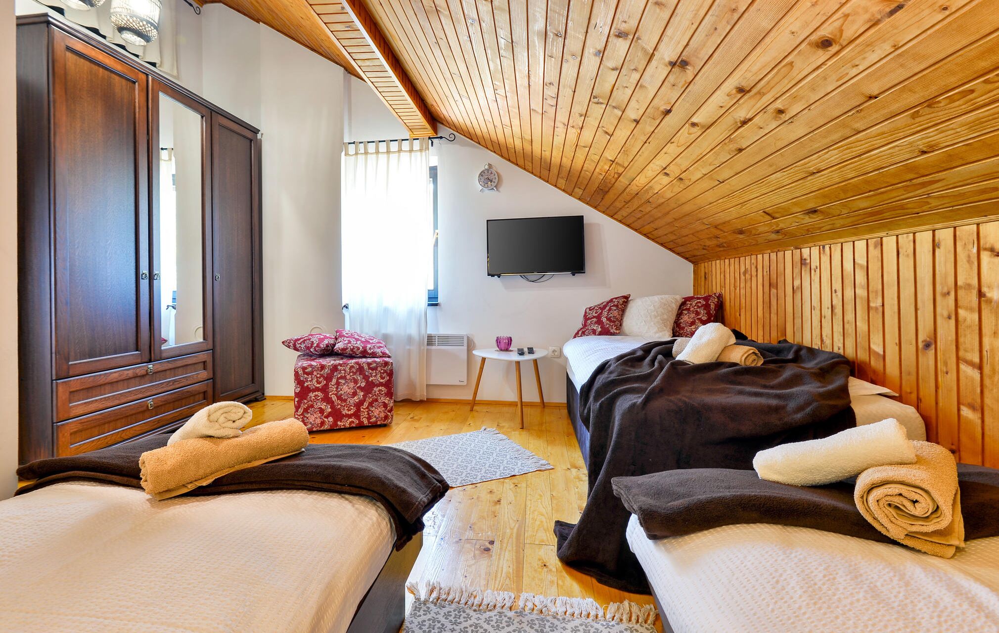 Ein gemütliches Schlafzimmer mit zwei Betten, einer Holzbalkendecke, einem Fernseher und einem Kleiderschrank.