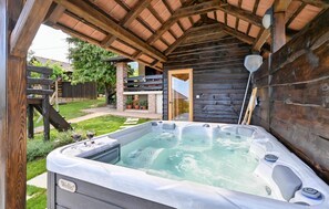 Relax in the hot tub on the covered patio, surrounded by a well-maintained lawn and a wooden fence.