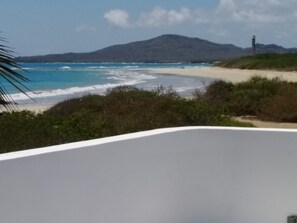 A beach view with a white bathtub in the foreground, a sandy beach, and a lighthouse in the distance.