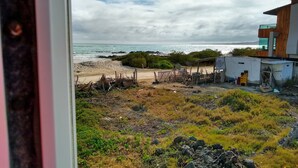 A coastal view with a sandy beach, rocky outcrops, and a building with a wooden facade. - Drake Inn (Puerto Villamil)