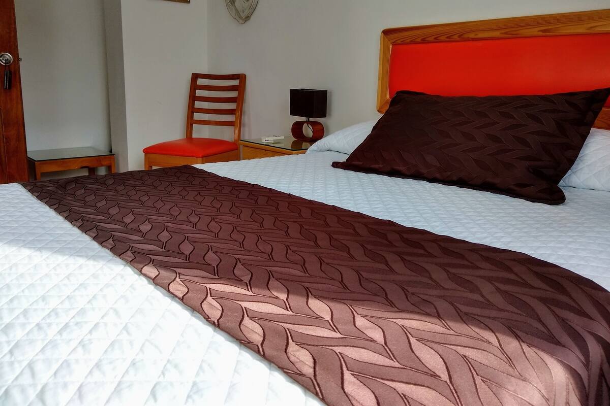 A neatly made bed with a patterned bedspread, a wooden headboard, and a single red chair in a room with a simple decor.