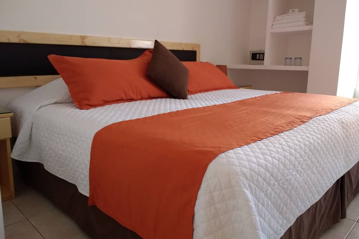 A bed with white and orange bedding, a wooden headboard, and a nightstand.